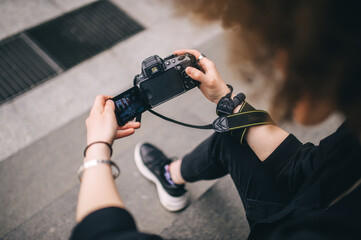 Close up view of female photographer holding digital camera while sitting on stair.