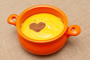 Homemade sweet corn pudding known in Brazil as Curau or Canjica Nordestina in ceramic bowl. Powdered cinnamon in the heart shape. Isolated on jute background. Close-up.