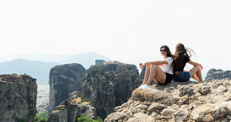 Two sisters sitting at the cliff with breathtaking view at landscape of Meteora, Greece.