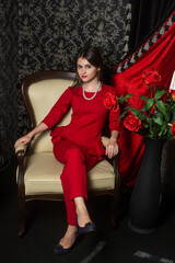 Girl in a red suit. The girl is sitting on an armchair. Elegant style