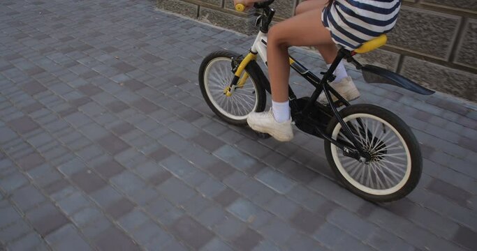 Unrecognizable girl  riding a bicycle along the city street wearing  striped shorts, white snickers and white T-shirt. Close up legs and bicycle. 50 fps slow motion 4k