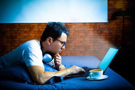 young asian man staring at laptop computer screen in bedroom at night. eye problems concept
