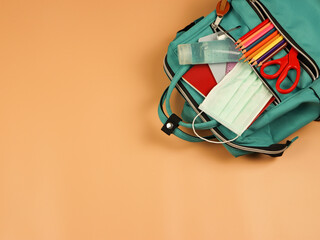  backpack with school supplies , surgical mask and alcohol sanitizer gel on orange background with copy space. COVID-19 prevention while going back  to school  and new normal  concept.