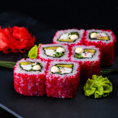 Japanese Sushi in red flying fish roe isolated on dark background. California roll with salmon, cucumber, avocado wrapped in nori seaweed and rice. Dish isolation