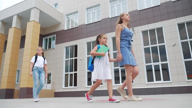 parent leads to school child with backpack back view. kids go to school with backpacks education concept. mom leads daughter by hand to first lesson. group school lifestyle girl children walk to class