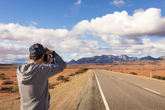 Male tourist taking pictures of the mountains at Ikara Flinders Ranges National Park. Panorama road heading to the ranges. Man wears neutral casual clothes and a cap. South Australia near Adelaide