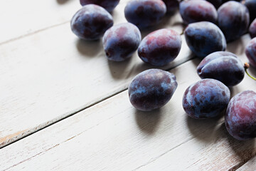 Ripe blue plums on white wooden table, copy space