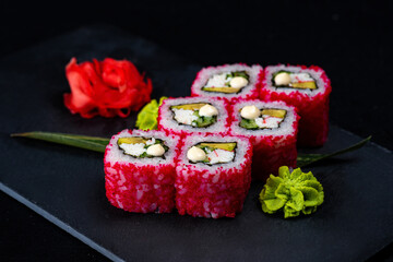 Japanese Sushi in red flying fish roe isolated on dark background. California roll with salmon, cucumber, avocado wrapped in nori seaweed and rice. Dish isolation