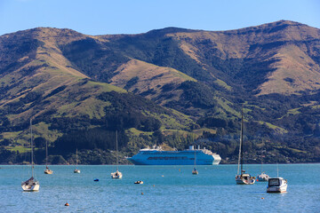 Fototapeta na wymiar A cruise liner in Akaroa Harbour, New Zealand, surrounded by a mountainous coastline and yachts