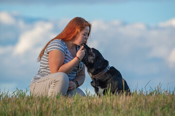 Plump young red-haired blue-eyed girl with a labrador retriever photographed on a field against a background of clouds.