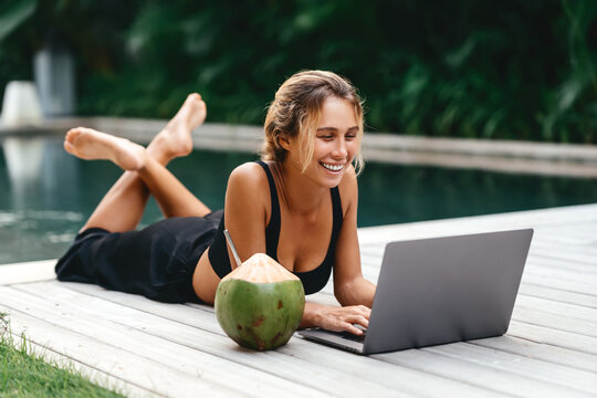 Attractive young female sitting in the swimming pool and working on a laptop