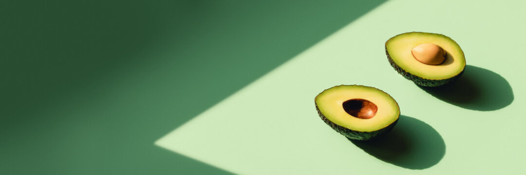 Avocado cut in half on a neo-mint background. Web banner with sunlight.