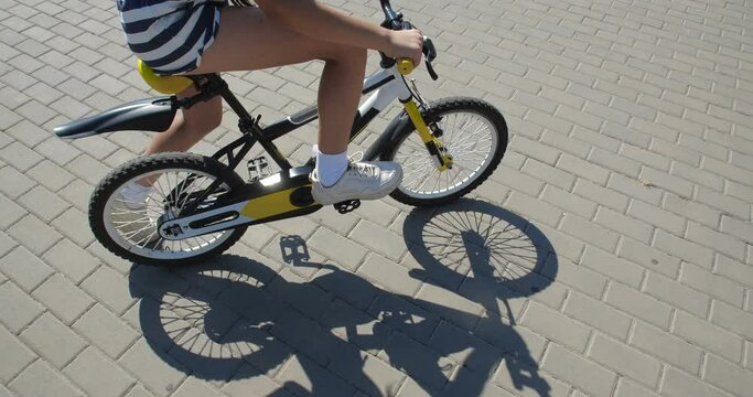 Unrecognizable girl  riding a bicycle along the city street wearing  striped shorts, white snickers and white T-shirt. Close up legs and bicycle. 50 fps slow motion 4k