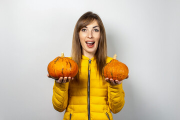 happy young girl in a yellow jacket holds two pumpkins on a light background. Halloween concept, autumn, celebration