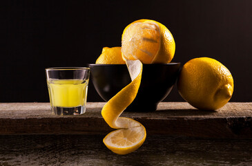 Lemon-flavored Italian liqueur Limoncello and bowl with lemons on wooden table background. Lemon...