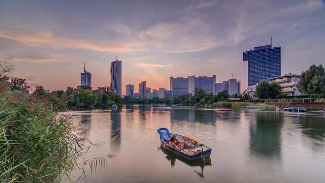 Sunset over Vienna international center skyscrapers with Kaiserwasser lake reflection view timelapse, Donaucity in capital of Austria. Colorful sky with clouds. Boat floating on water