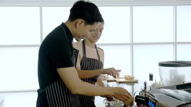 Multi ethinic colleague working together in cafe concept. Hand held, medium shot of male asian barista preparing coffee while female caucasian colleage teaching, giving comment and support