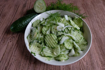A delicious salad of fermented cucumbers with onions and dill in a white plate on a wooden background. Concept -home-made for the winter. Healthy diet.