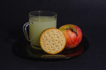 there is an apple, cookies and a transparent cup with dry fruit juice on the plate