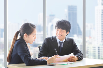 Asian business people wearing formal suit are discussing over the annual report in formal business office with modern cityscape on the background with copy space