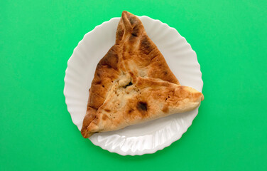 Famous traditional Arabic, Middle East, Israel cuisine. Spinach Manakish on a green background. Spinach triangle pie on white plate