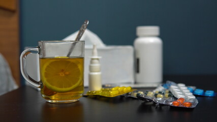 A woman takes a glass of tea with lemon. Medication on the table.