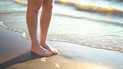 A young woman stands barefoot on the sandy seashore. Legs close up.