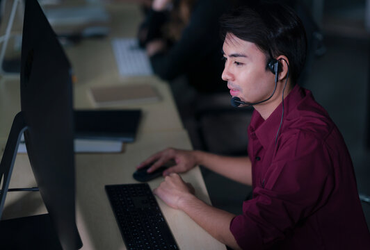 Thai Asian man customer services care operators working night shift in call center for helping assistance client in workplace at night time, Friendly helpdesk operator working at night