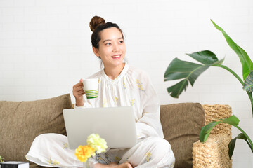 ソファーの上であぐらをかいてパソコンを操作する女性