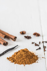 Baking spices like cinnamon, star anise, and vanilla bean on white wooden table. Vertical stock photo with copy space.
