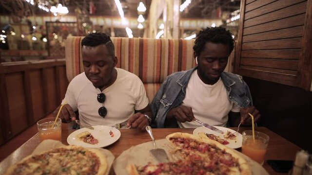 African men friends eating pizza in restaurant