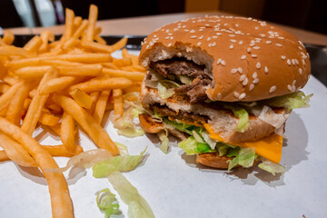 Close up of a bitten double cheeseburger on a tray with freshly cooked french fries inside a fast food restaurant in shopping mall