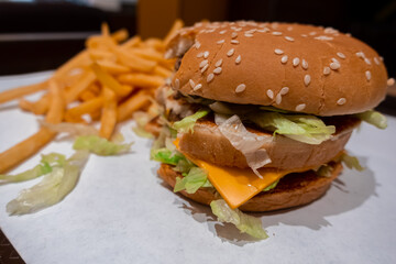 Close up of a bitten double cheeseburger on a tray with freshly cooked french fries inside a fast food restaurant in shopping mall