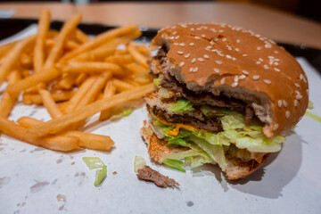 Close up of a bitten double cheeseburger on a tray with freshly cooked french fries inside a fast food restaurant in shopping mall