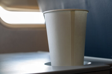 Paper cup with drink on board in flying aircraft. Refreshment drink on desk in the airplane. Coffee in paper cup on table in air plane.