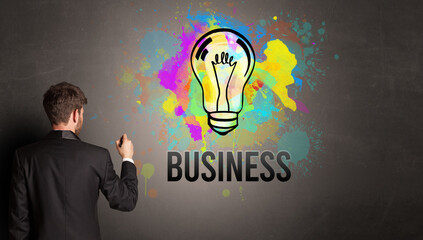 businessman drawing colorful light bulb with BUSINESS inscription on textured concrete wall, new business idea concept