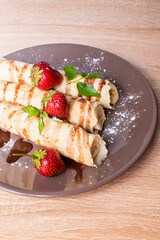 Pancakes with banana and strawberries on a plate. Banana wrapped in a pancake and with strawberries on top. Breakfast with Pancakes with berries and banana and chocolate..