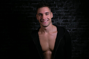 Portrait of handsome smiling young man looking at camera with open black shirt revealing muscular pecs and sixpack abs