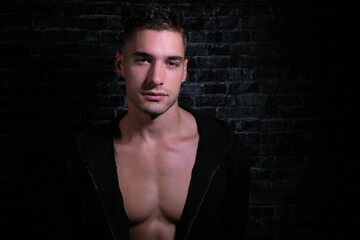 Portrait of handsome serious young man looking at camera with open black shirt revealing muscular pecs and sixpack abs