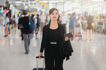 Asian businesswoman walking with a luggage at airport terminal and airport terminal blurred crowd of travelling people on the background.