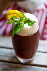 Foamy Iced Tea with Mint Leaves in served with Big Glass / Ice Tea Foam on Wooden Table.