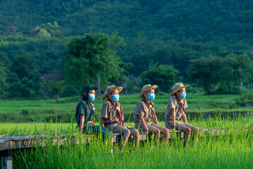 Group of America boy scouts wearing protective mask to Protect Against Covid-19 sitting in green field.