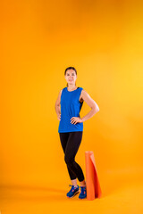 Fototapeta na wymiar Full-length sporty girl with a fitness Mat on an orange background