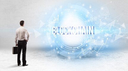 Rear view of a businessman standing in front of BLOCKCHAIN inscription, modern technology concept