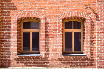 An old red brick wall with two Windows.