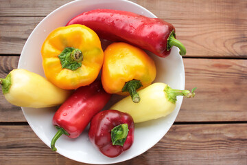 Red, orange, and yellow bell peppers on the white plate. Fresh vegetables on a wooden table. Top view, copy space