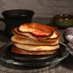 Several pancakes with cherry jam on wood background