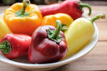Red, orange, and yellow bell peppers on the white plate. Fresh vegetables on a wooden table. Top view, copy space