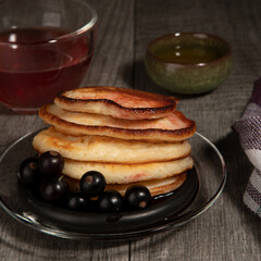 Several pancakes with black currant and tea on wood background