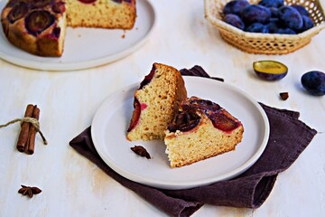Sliced round honey cake or muffin with fresh plums on a light grater on a light concrete background. Plum baked goods.